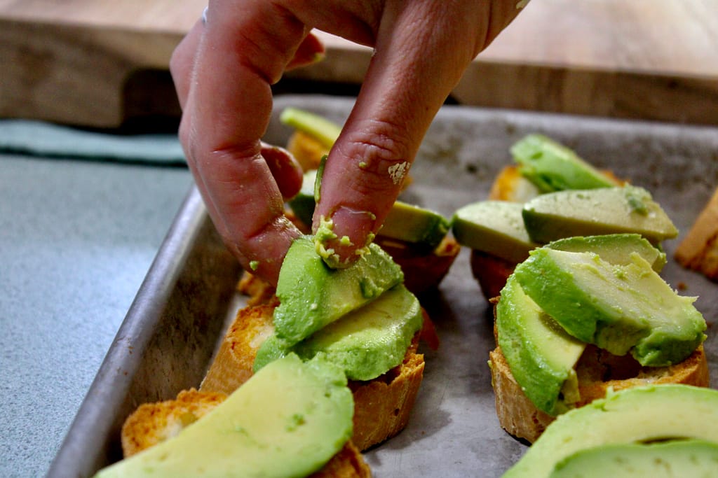 Layering avocado slices on top of sliced baguettes.
