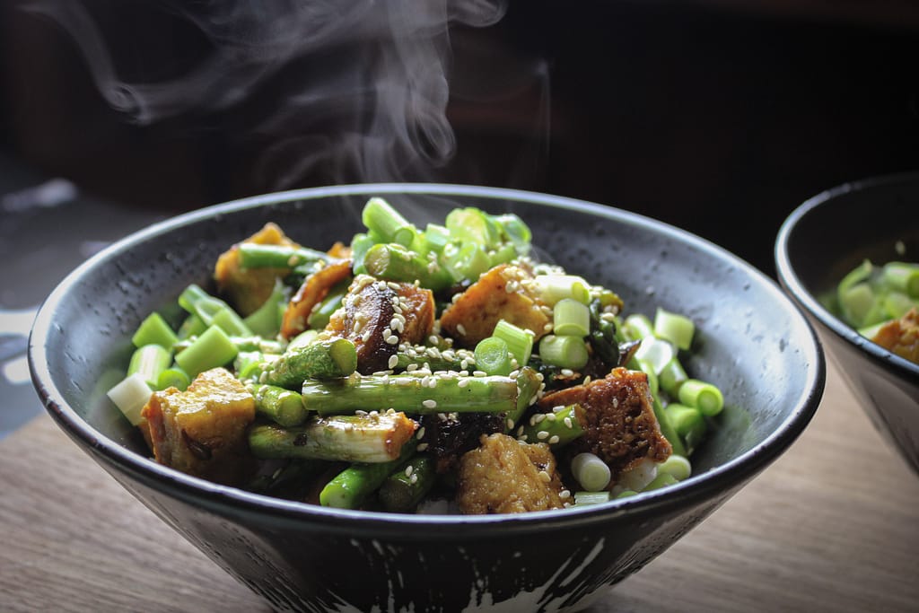 A steaming bowl of stir fry in a black bowl.